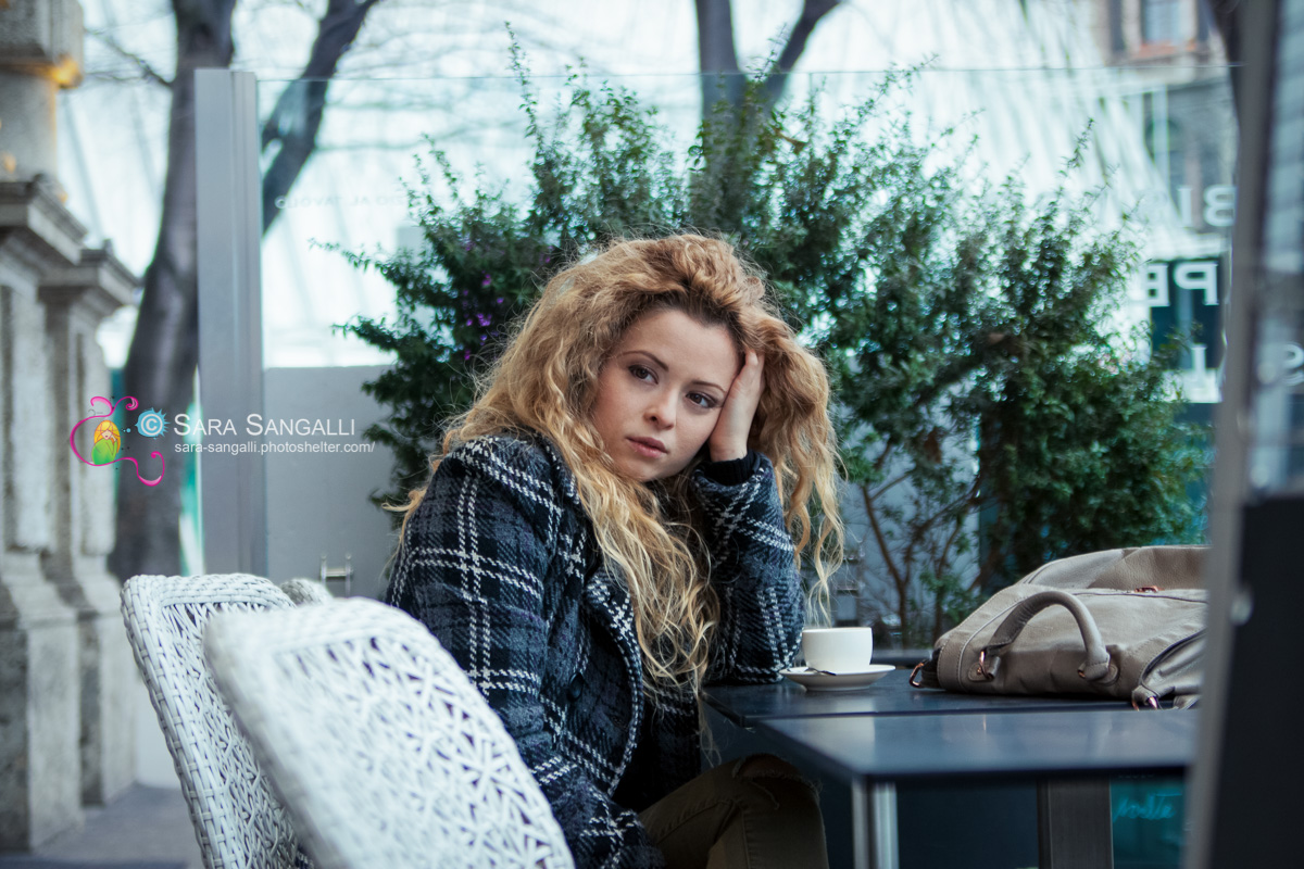 Young blonde woman taking a break at a coffee bar. Serious expression, looking away.