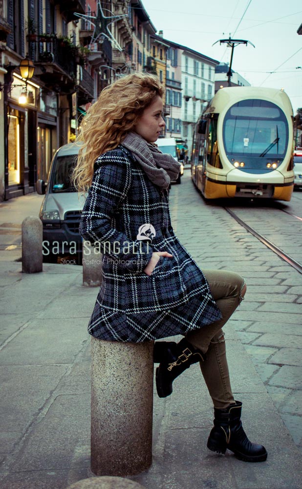 Blonde young woman in Milan, Italy, looking away from camera. Public transportation approaching from behind