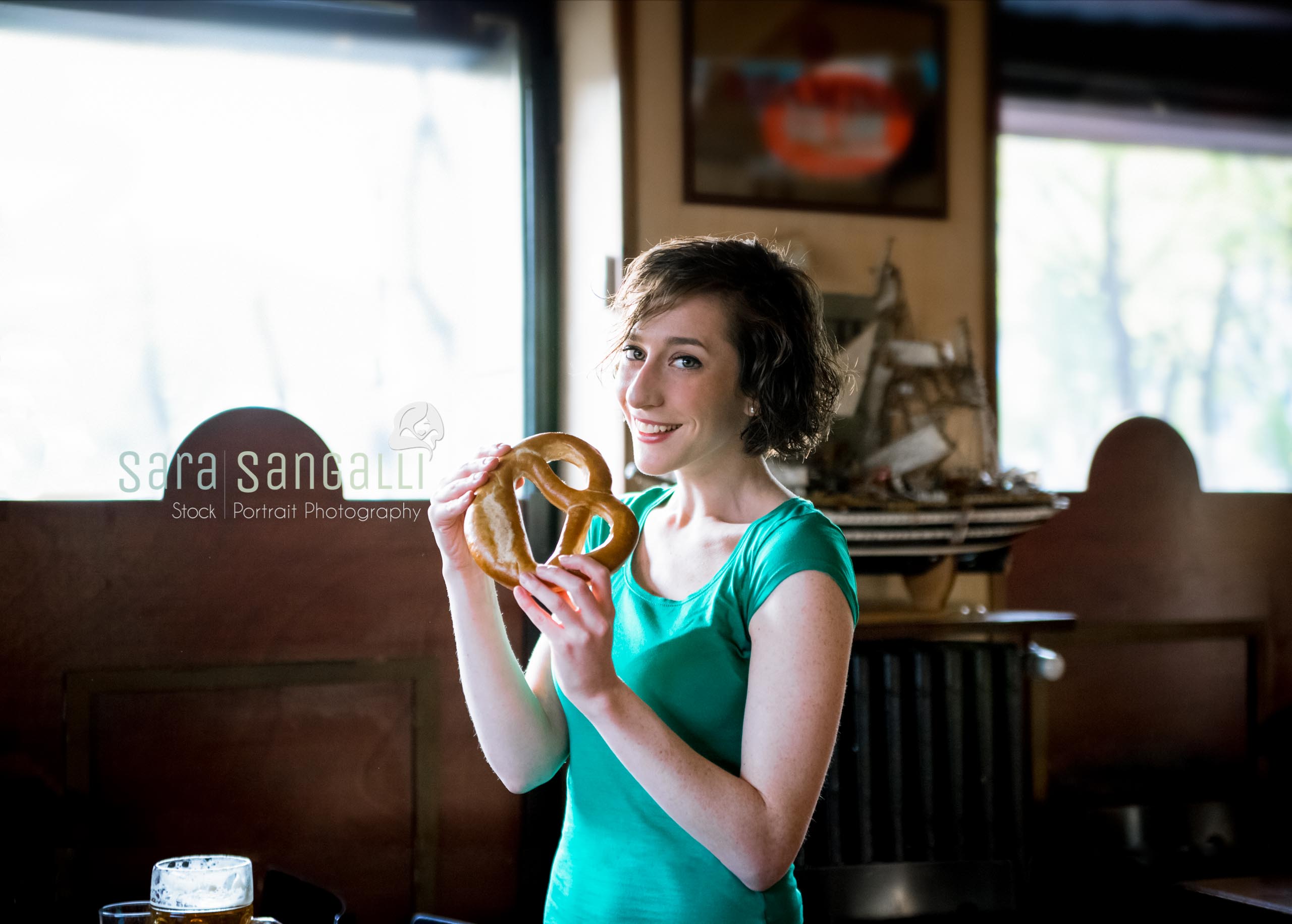 Young brunette woman about to eat a delicious pretzel, looing at camera, indoor setting