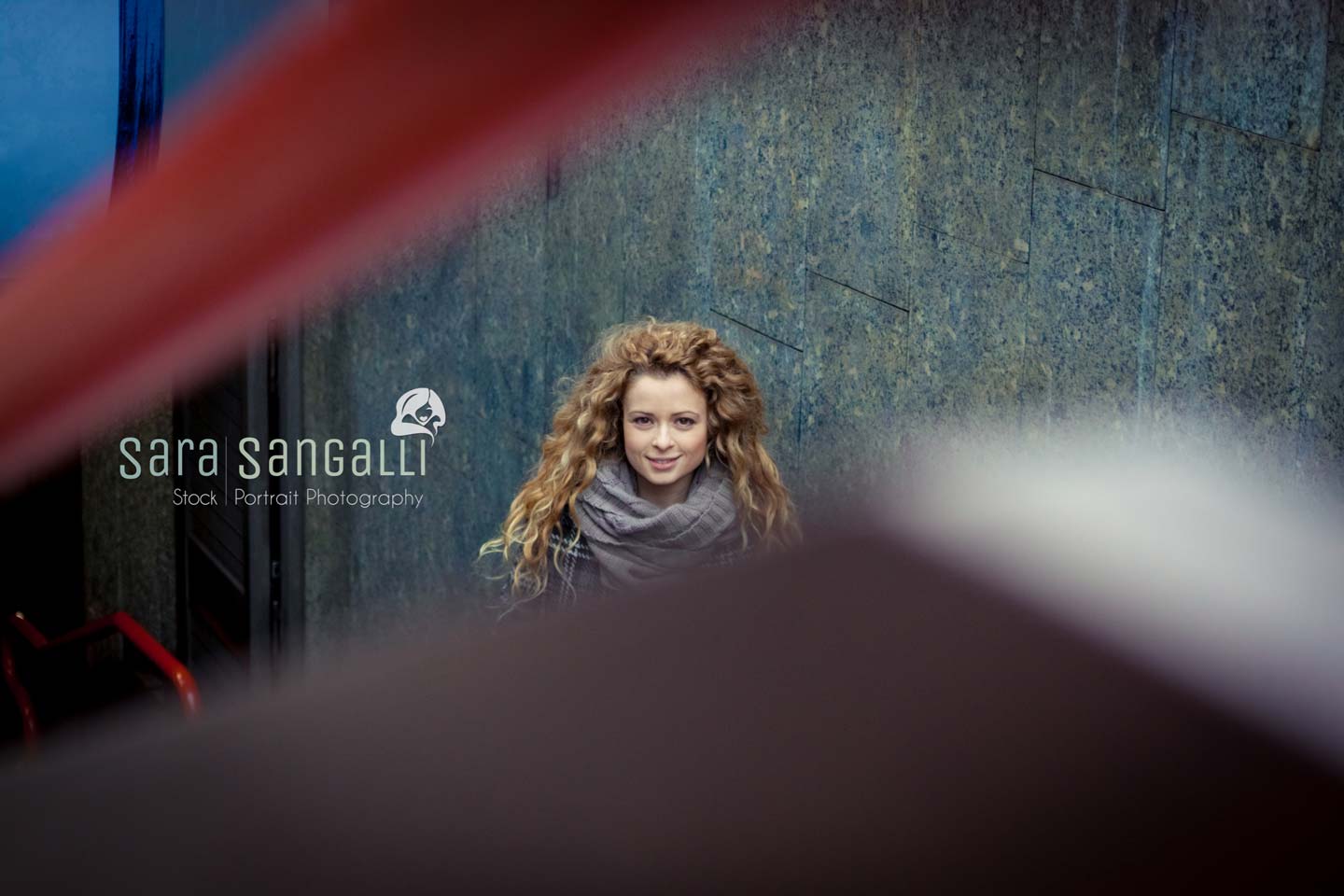 A blonde young woman watches into camera through a underground stairs handrail