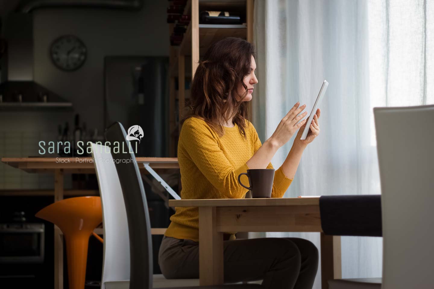 Young caucasian brunette woman using a tablet and sitting near a table. Indoor setting