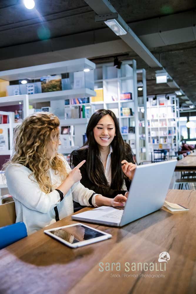 two female laughing and talking with each while watching at laptop screen in design studio