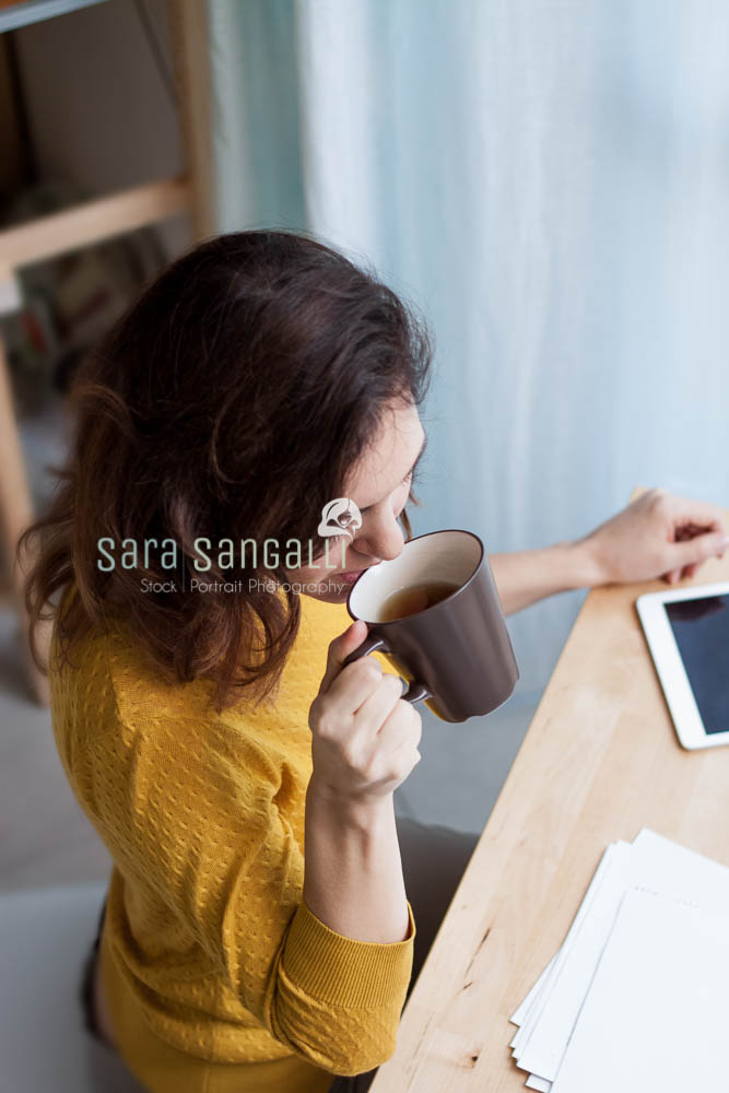 Young caucasian brunette woman taking notes and drinking tea. Indoor setting