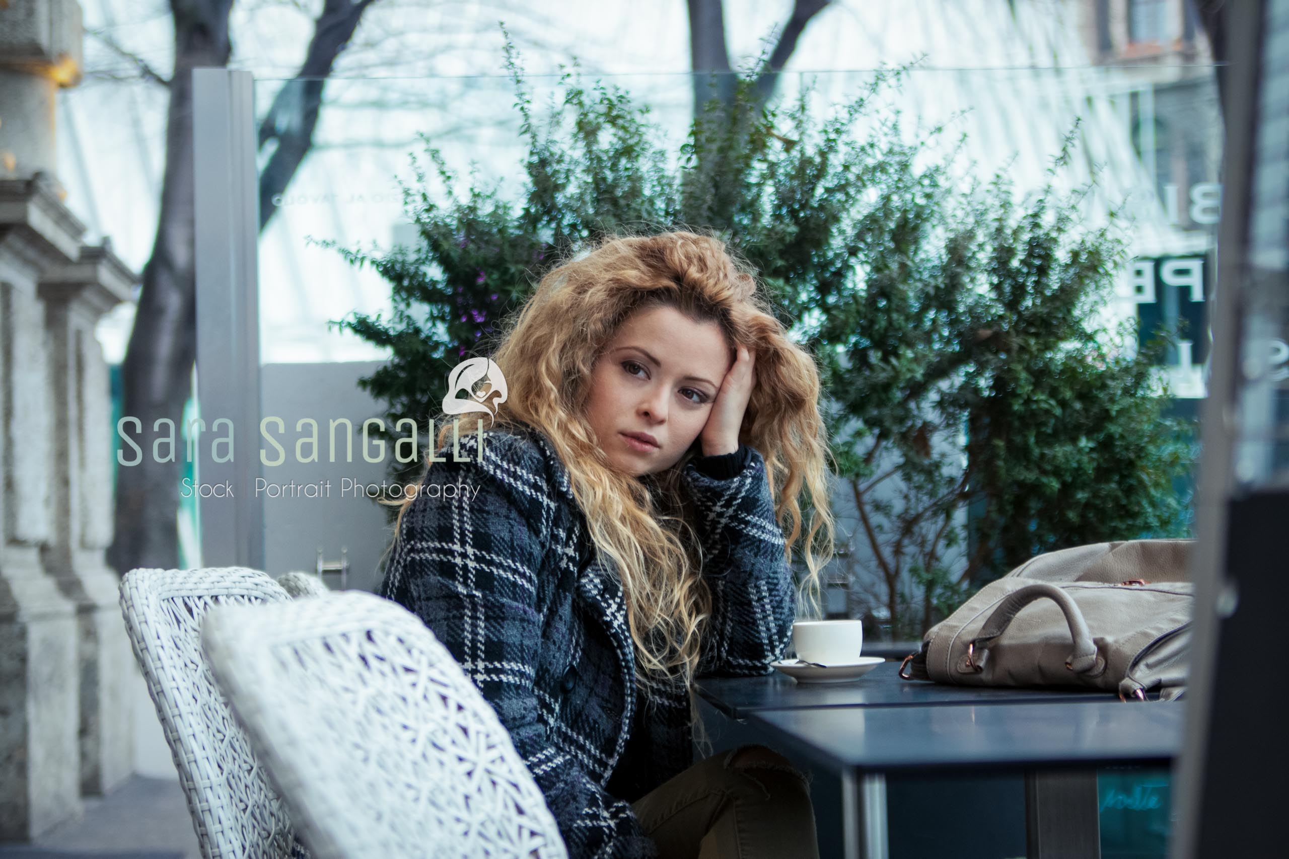 Young blonde woman taking a break at a coffee bar. Serious expression, looking away.