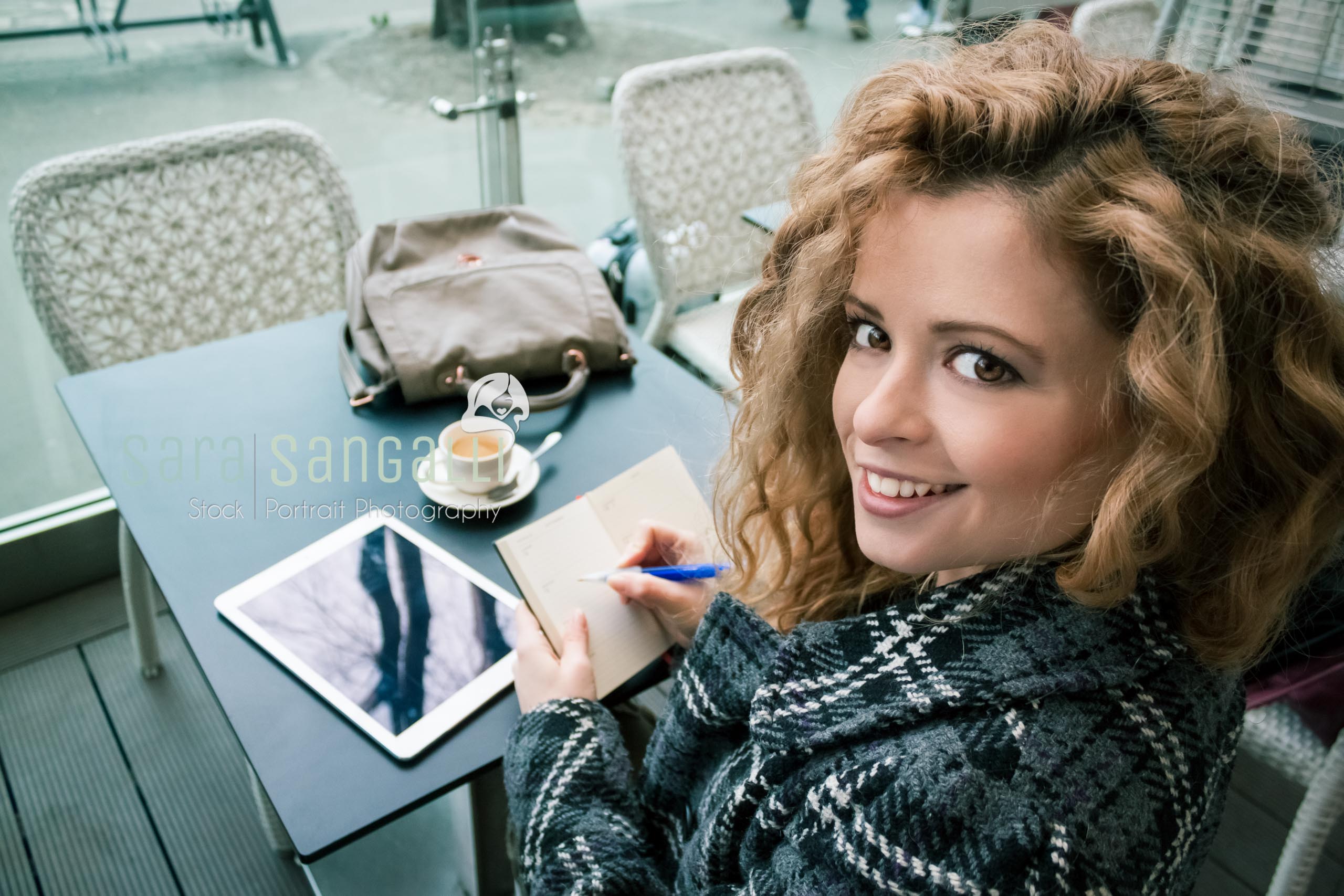 Young blonde woman taking a break at a coffee bar. Taking notes on a tablet and writing on her calendar