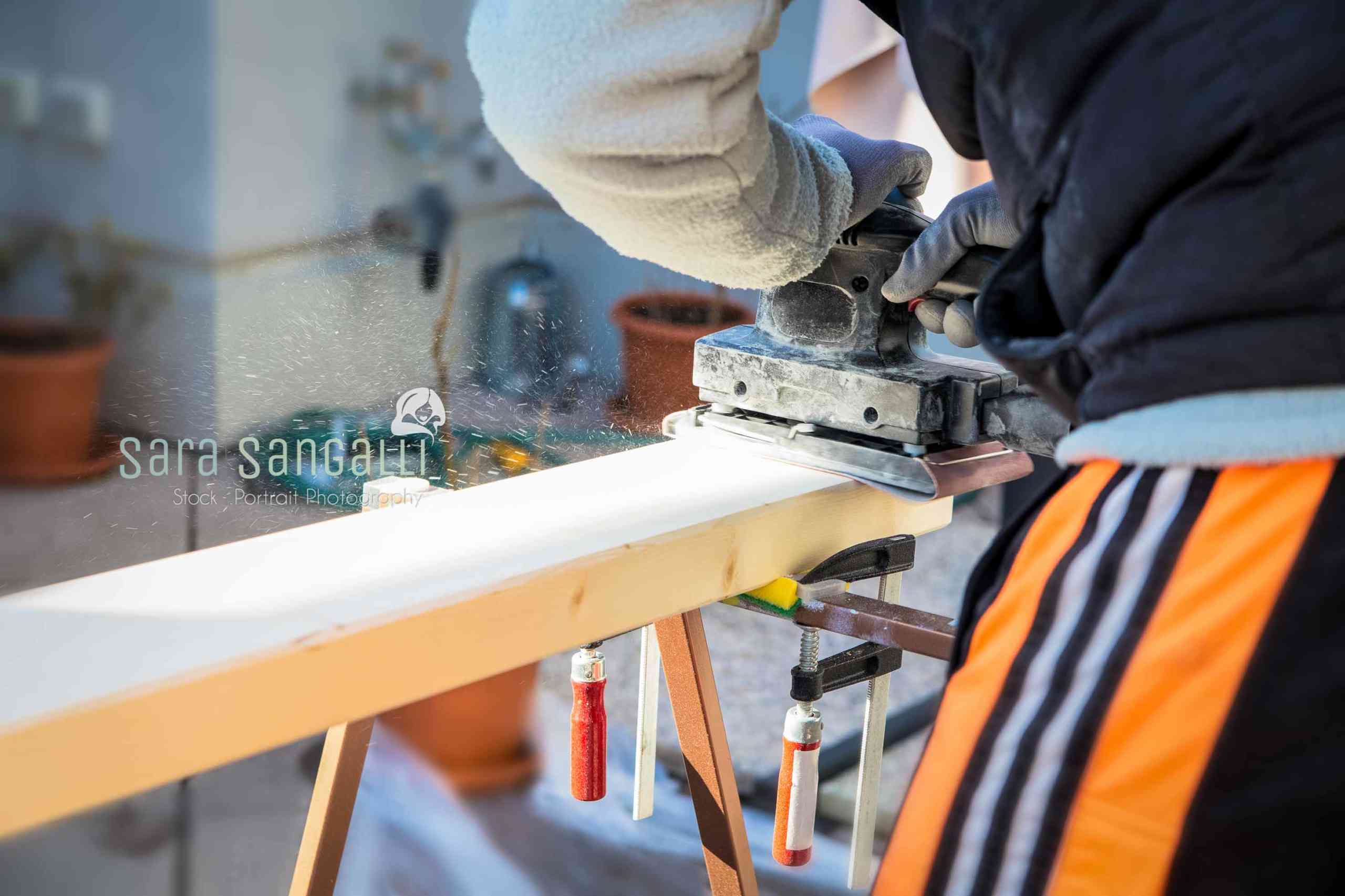 Men doing some woodwork, sanding a wood with sander