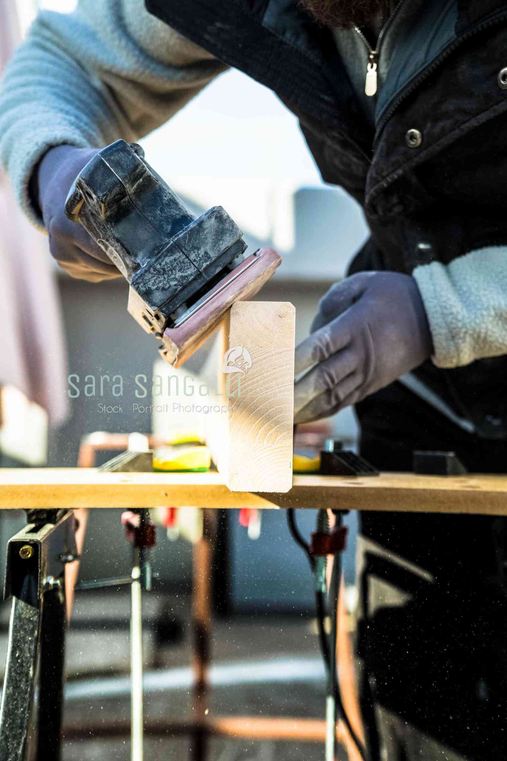 Men doing some woodwork, sanding a wood with sander