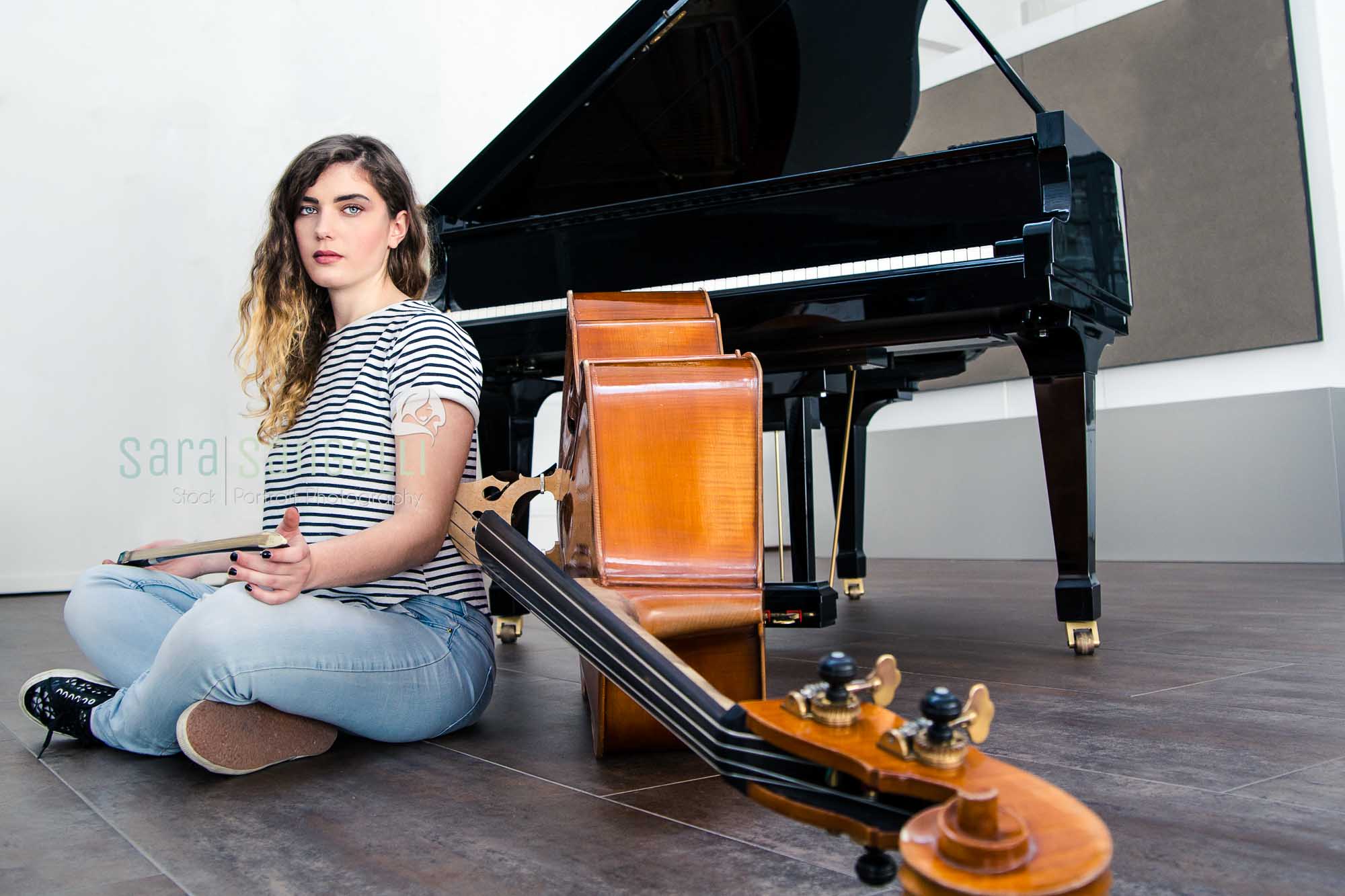 Young Double bass player sitting on the ground in front of a grand piano.